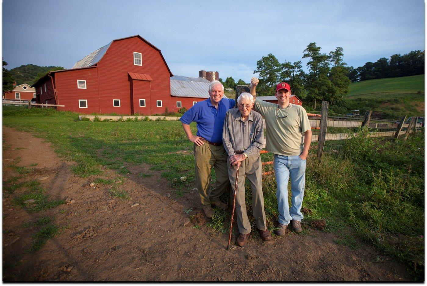 Three generations of Shipleys, Bob, R.G. at 102, and Gray, standing in front of the red barn
