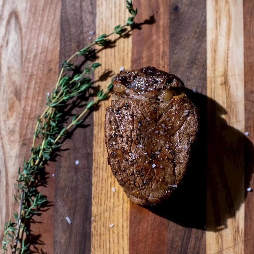 Cooked filet mignon on a cutting board with fresh thyme